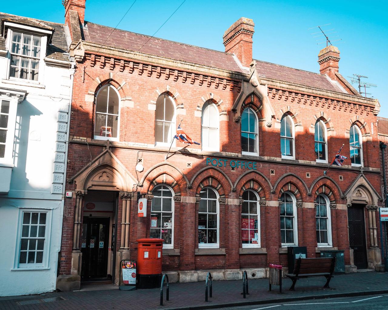 The Victorian red-brick frontage of Newport Pagnell Post Office on the High Street, with a Royal Mail pillar box outside
